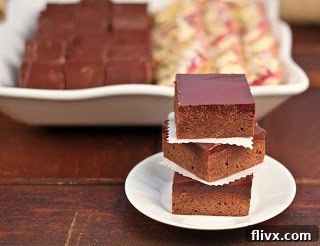 Ultimate Truffle Brownies with Loads of Chocolate and Ganache Three perfectly stacked truffle brownies, generously topped with chocolate ganache, on a pristine white plate.