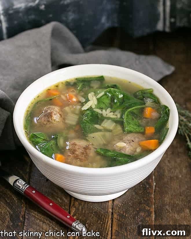 A beautifully presented bowl of Italian Wedding Soup, brimming with tender meatballs, vibrant greens, and pasta, with a red-handled spoon poised to take a spoonful.