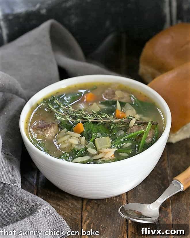 A close-up shot of a white bowl filled with steamy Italian wedding soup, featuring the texture of the meatballs, pasta, and greens, accompanied by a bamboo-handled spoon.