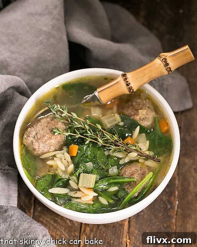 An overhead view of a steaming bowl of Italian Wedding Soup, with a bamboo-handled spoon lifting a meatball, highlighting the fresh ingredients and rich broth.