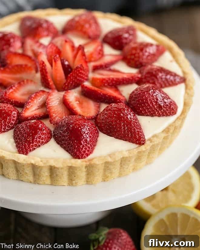 A beautifully arranged Strawberry Lemon Tart on a pristine white cake stand, showcasing its vibrant red strawberries and golden lemon filling.