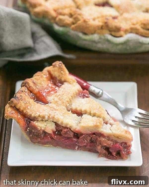 A perfectly baked slice of Classic Rhubarb Pie, showcasing its vibrant filling and golden lattice crust, served on a crisp white dessert plate.