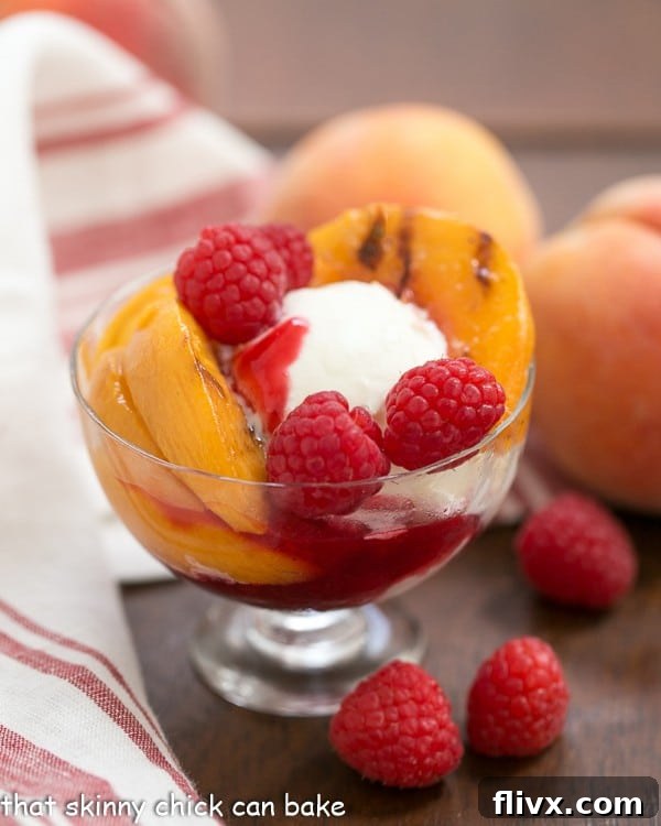 Grilled Peach Melba in a glass serving dish with a red white napkin, peaches, and fresh raspberries.