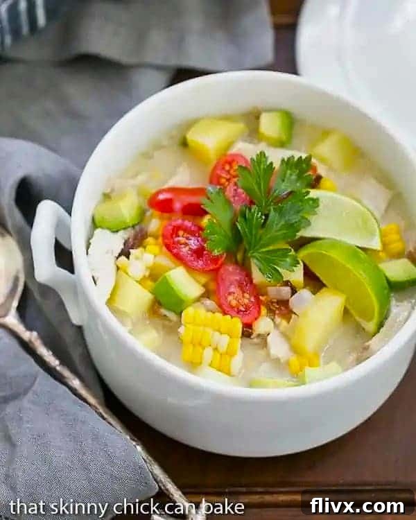 A white soup tureen filled with corn chowder, garnished with fresh herbs and tomatoes.