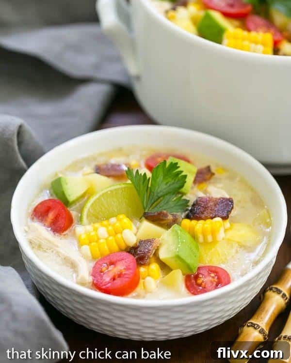 A white bowl filled with corn chowder with a large pot behind it, ready to serve.