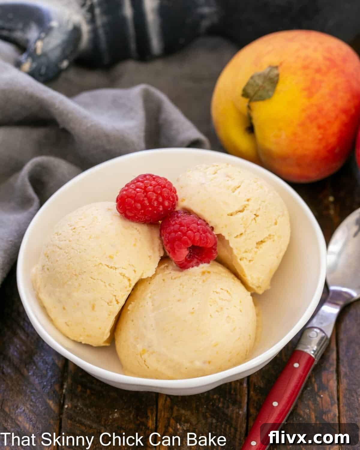 A shallow bowl filled with creamy, light orange No-Churn Roasted Peach Ice Cream, garnished with fresh raspberries.