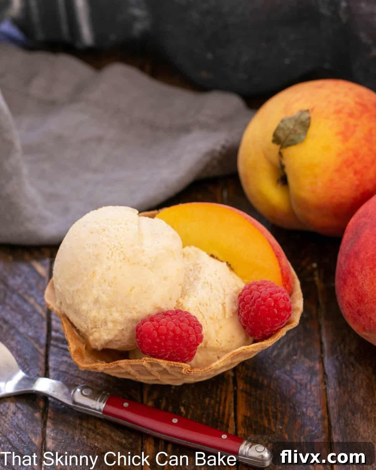 A scoop of no-churn peach ice cream served in a sugar cone bowl, adorned with fresh raspberries and thin peach slices.