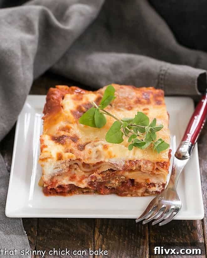 A delicious serving of Lasagna with Italian Sausage, glistening with melted cheese and rich sauce, on a white plate, accompanied by a red-handled fork, ready to be enjoyed.