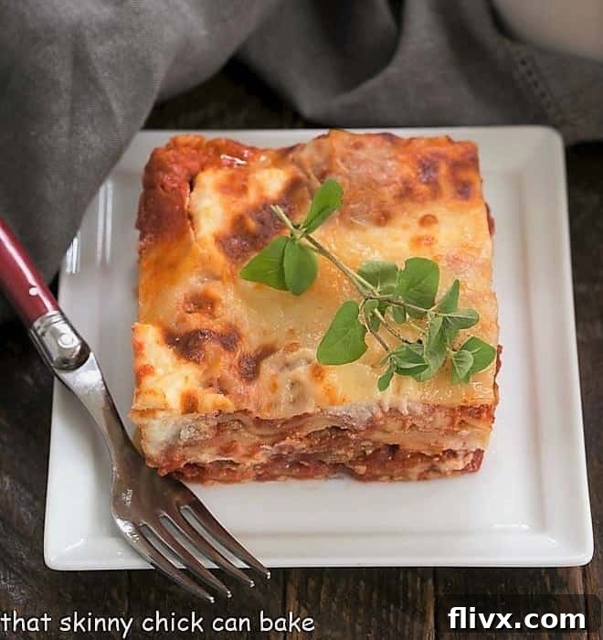 A perfectly cooked slice of ricotta lasagna on a square white plate, showing distinct layers of pasta, cheese, and meat sauce.