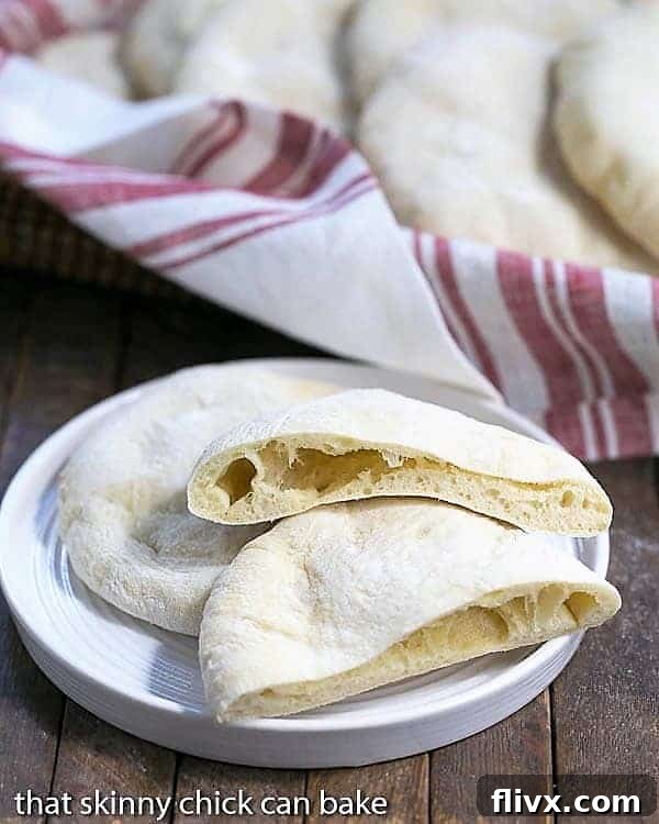 Freshly baked homemade pita bread on a white ceramic plate, with one sliced in half to show the perfect pocket.