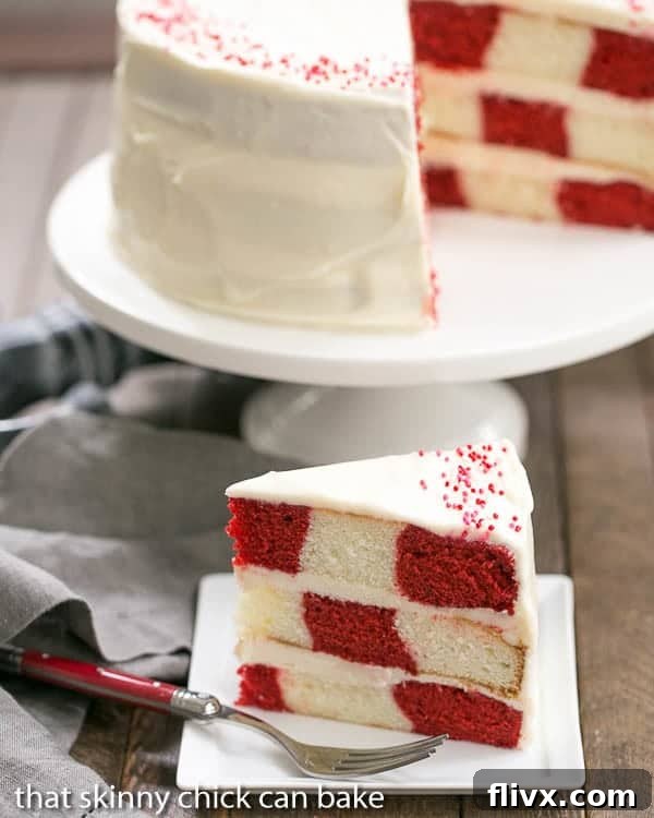 A beautiful Red Velvet Checkerboard Cake on a stand with a perfectly cut slice revealing the distinct red and white checkered pattern, inviting indulgence.