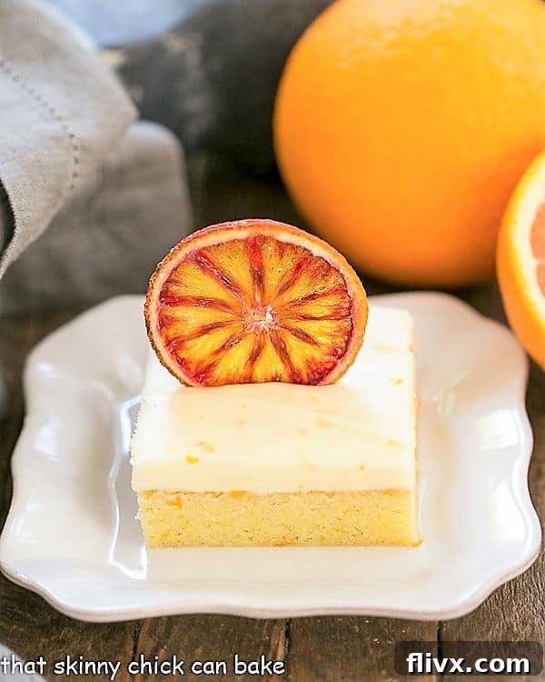 Rich Orange Cake with Cream Cheese Frosting on a square white plate, garnished with fresh orange slices
