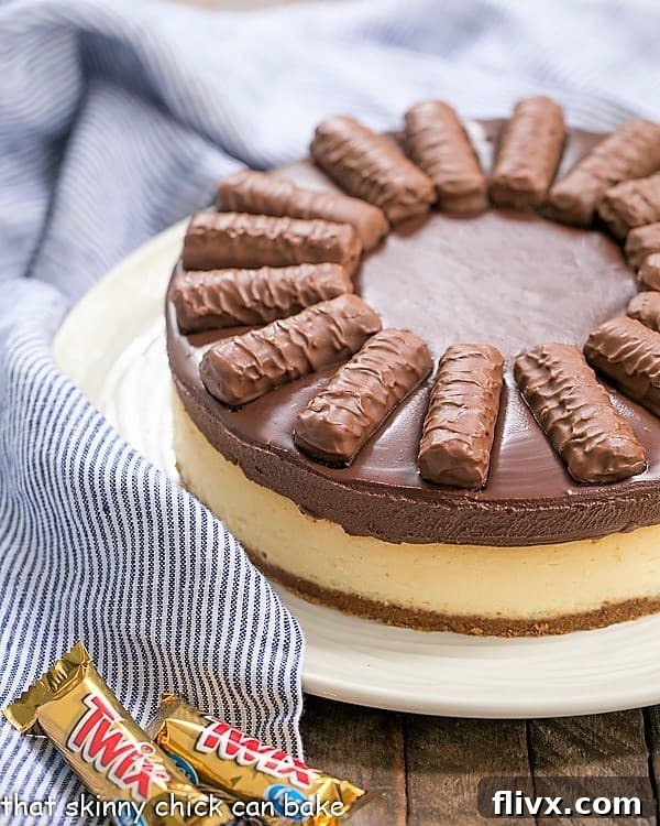A whole Chocolate Caramel Twix Cheesecake on a serving plate, showing off its generous topping of chocolate ganache and a hint of a crumbly crust.