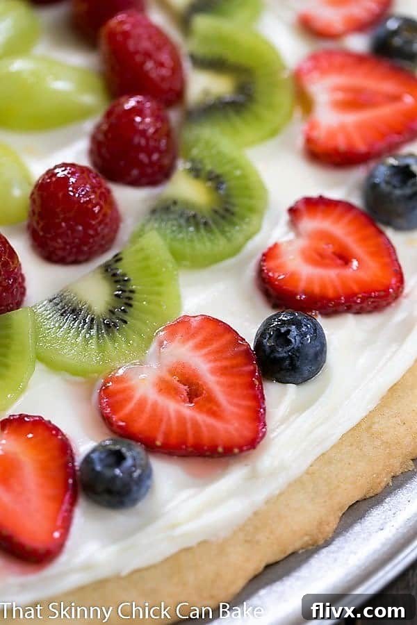 Close view of the fruit on a Fresh Fruit Pizza, showcasing blueberries, raspberries, kiwi, and sliced strawberries on a creamy frosting.