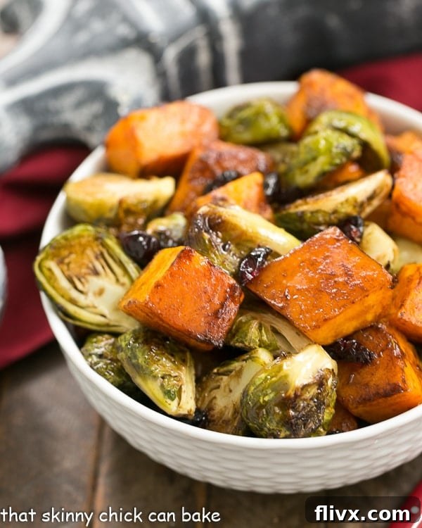 A beautiful medley of Roasted Autumn Vegetables, featuring golden butternut squash, green Brussels sprouts, and ruby-red dried cranberries, served in an elegant white basketweave bowl.