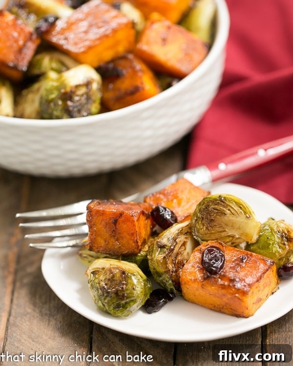 A small white plate holds a portion of Roasted Autumn Vegetables, with a larger bowl of the same vibrant medley blurred in the background, inviting a closer look.