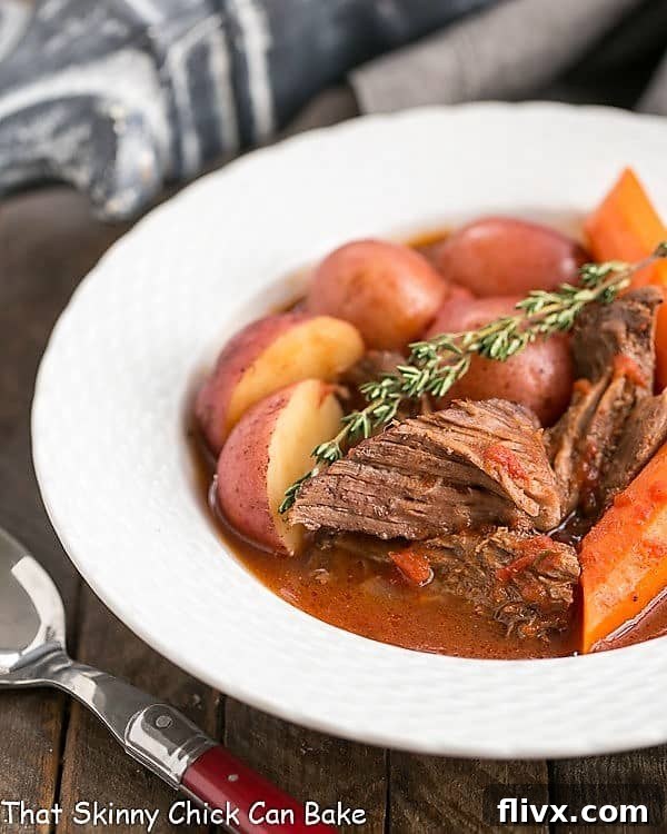 A perfectly cooked easy pot roast served in a shallow white bowl, garnished with a fresh sprig of thyme. The beef is tender and surrounded by vibrant carrots and potatoes, sitting in rich, savory pan juices.