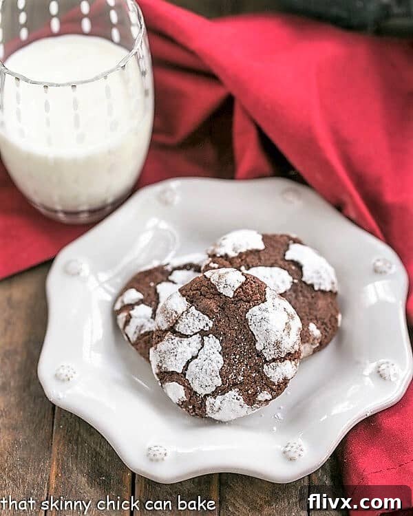 Close-up of freshly baked Chocolate Crackle Cookies on a decorative white plate, showcasing their signature crackled tops dusted with powdered sugar.