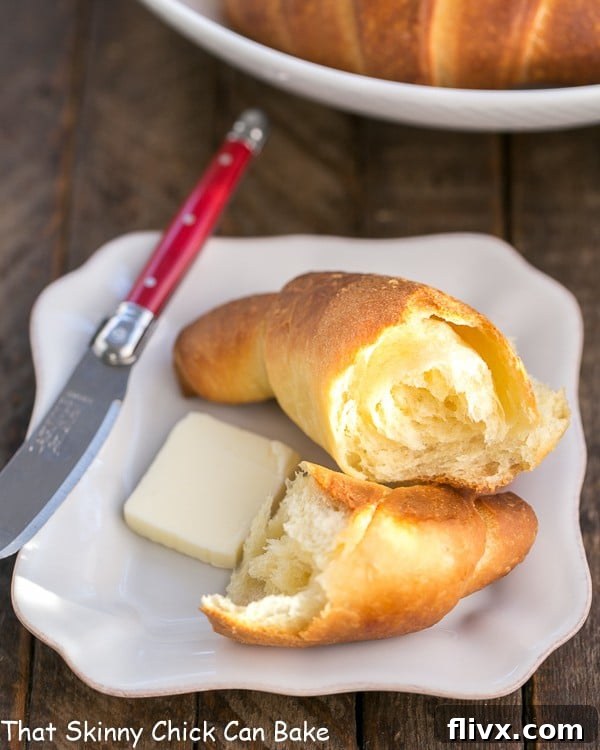 Buttery Homemade Crescent Rolls on a white plate with a red handled knife, showcasing their golden-brown exterior and flaky texture.