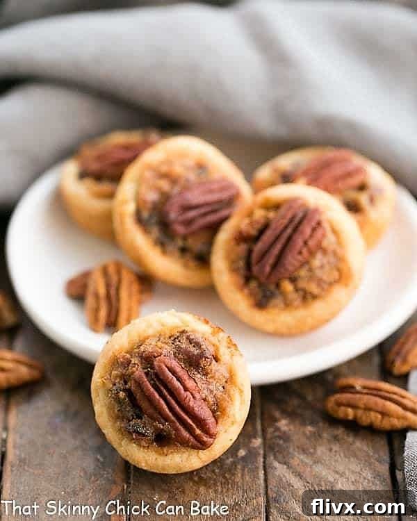Pecan Tassies on a white plate with pecan halves, showcasing their golden crusts and rich filling.