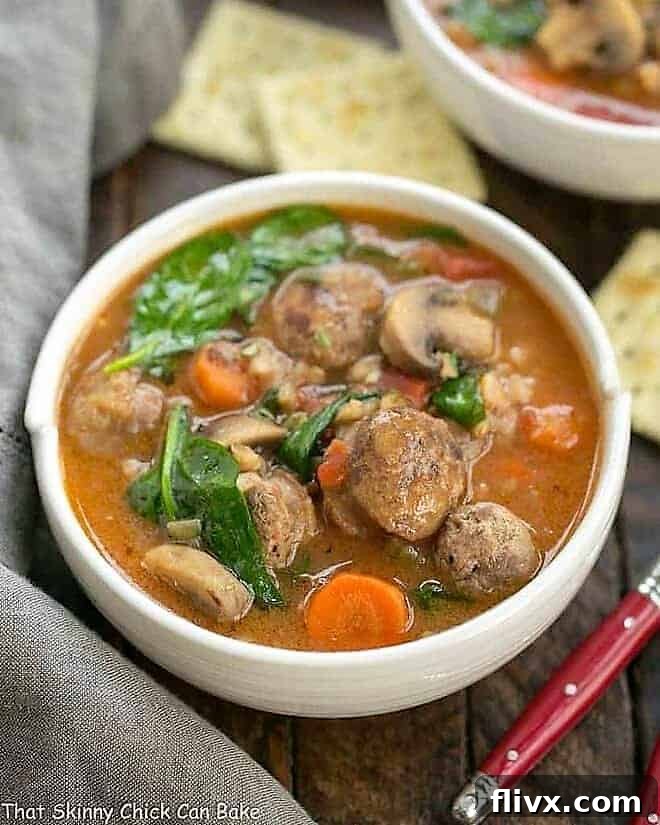 A steaming bowl of Rustic Farro Soup, brimming with tender farro, savory sausage, and vibrant vegetables, garnished with fresh herbs and a red-handled spoon beside it, inviting a cozy winter meal.