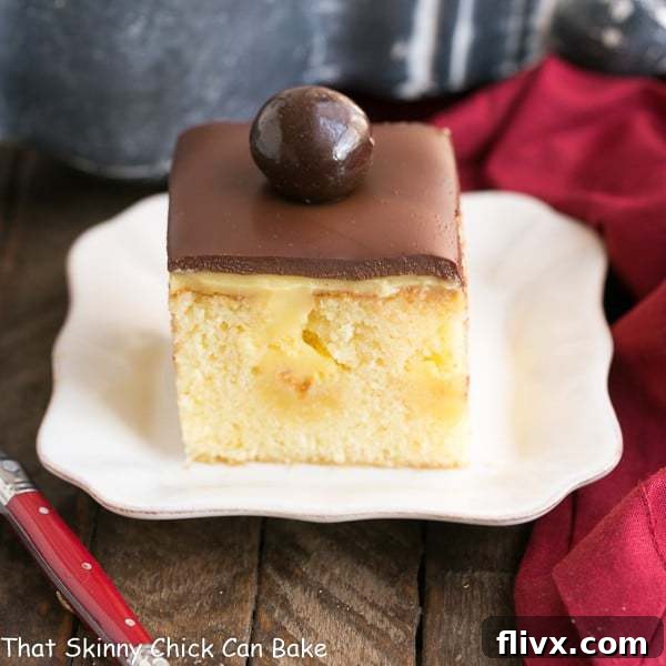 A slice of Boston Cream Pie Poke Cake on a white plate, showcasing the layers of cake, pudding, and ganache