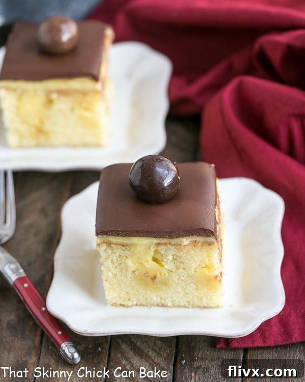 Two white dessert plates featuring slices of Boston Cream Pie Poke Cake, showing the distinct layers