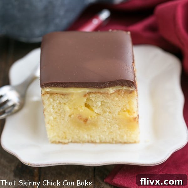 A close-up of a slice of Boston Cream Pie Poke Cake, revealing the moist cake, creamy pudding, and rich ganache layers