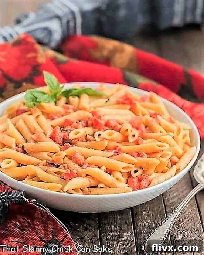 Penne alla Vodka in a white ceramic bowl with a sprig of basil.