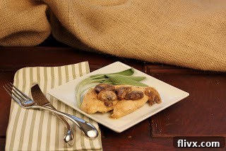 Close-up of a plate of chicken marsala with succulent chicken breasts and a rich mushroom sauce, garnished with sage leaves on a green and white striped napkin.