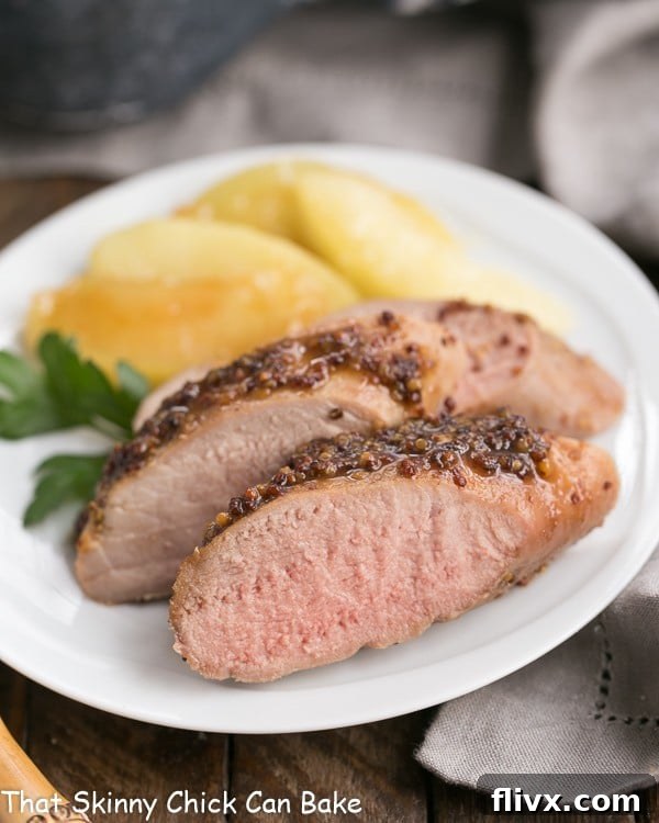Close up of a plate of apple mustard pork tenderloin with apple slices and a rich glaze.