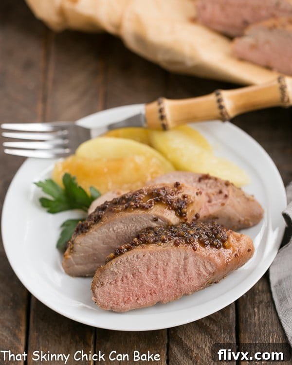 A plate of perfectly sliced apple mustard pork tenderloin with a bamboo handle fork.