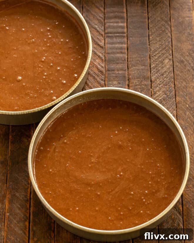 Cake batter being divided evenly between two prepared cake pans.
