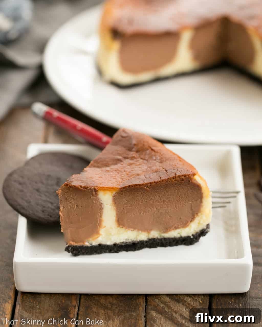 A perfectly sliced piece of Polka Dot Cheesecake on a square white plate, accompanied by two chocolate wafer cookies and a red-handled fork, highlighting its creamy texture and distinct chocolate dots.