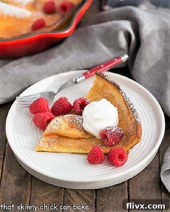 Best Dutch Baby Pancake slice on a white plate topped with cream and raspberries.