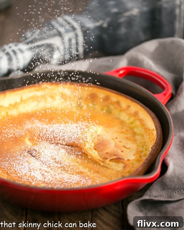 Best Dutch Baby Pancake in a red skillet with a dusting of powdered sugar.