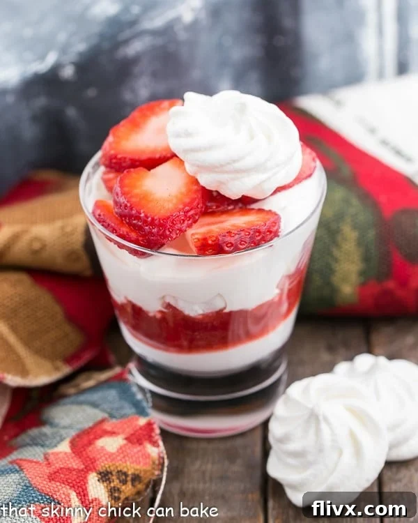 A beautifully presented Strawberry Eton Mess fruit parfait in a glass, topped with a delicate meringue cookie and artfully sliced fresh strawberries, showcasing vibrant layers.