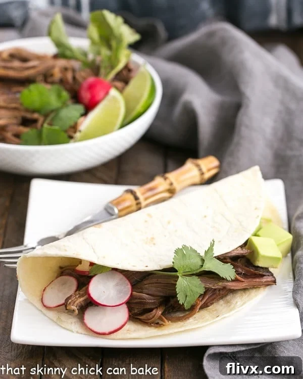 Slow Cooker Carne Asada in a tortilla on a square white plate, garnished with fresh cilantro.