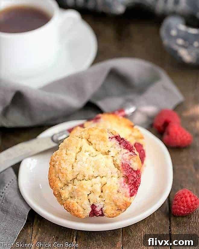 Three Raspberry Cream Scones artfully arranged on a round white plate, accompanied by a steaming cup of tea.