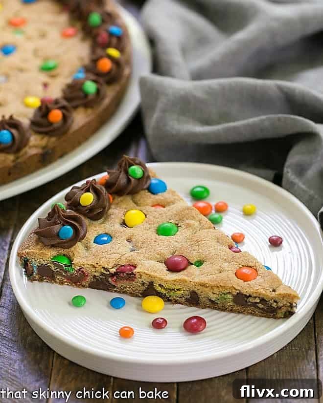 A perfectly baked wedge of homemade chocolate chip cookie cake, adorned with colorful M&M's, rests invitingly on a pristine white plate, ready to be enjoyed.