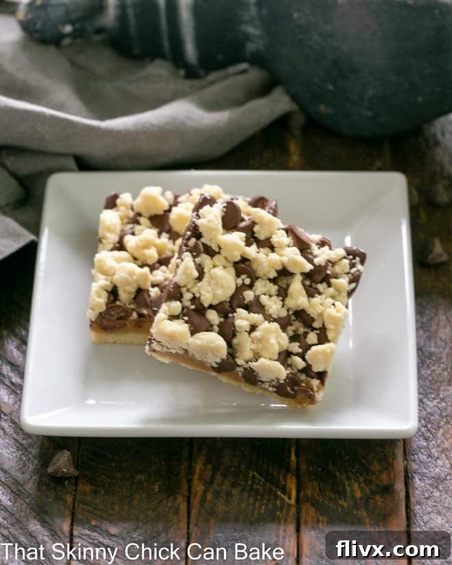 Two golden-brown chocolate caramel bars with streusel topping resting on a square white plate, ready to be enjoyed.