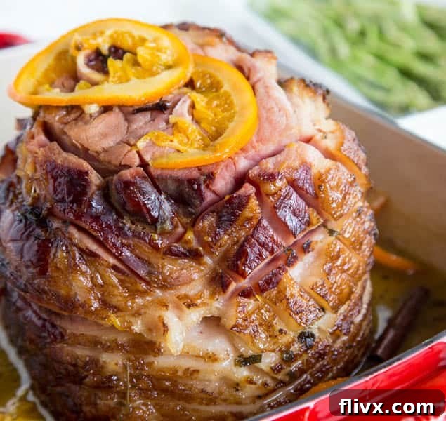 Delicious oven-baked ham with a sweet tangerine glaze, garnished with fresh herbs.