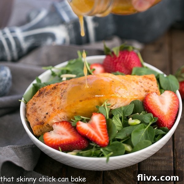 Fresh strawberry vinaigrette dressing pouring over a Salmon Watercress Salad in a pristine white salad bowl, highlighting its vibrant colors.
