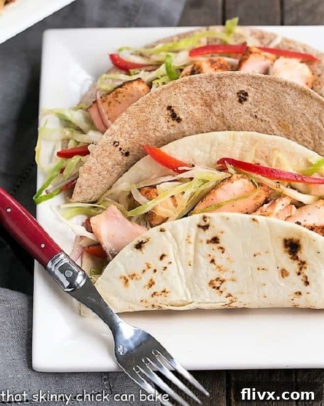 Two Salmon Tacos with Mango Salsa on a square white plate with a red handled fork. Delicious and healthy fish tacos.