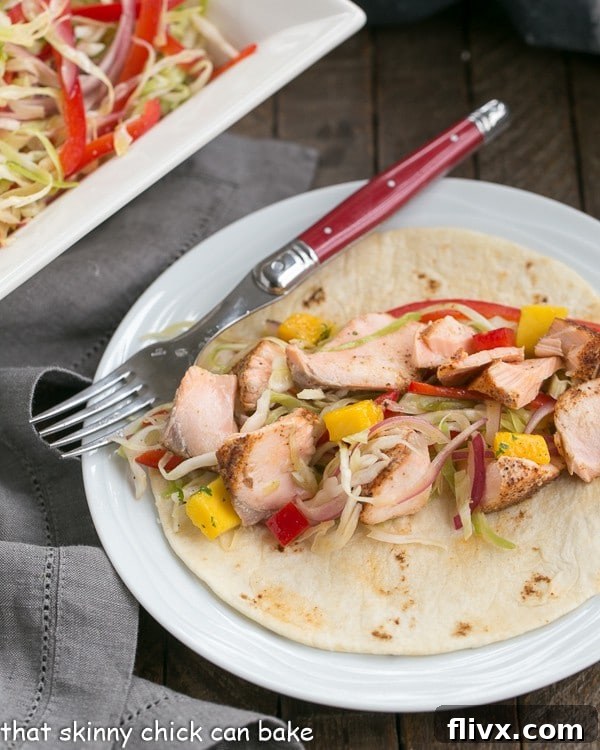 Fish Tacos Recipe with Salmon and Mango Salsa on a round white plate with a red handled fork. A close-up of the delicious fish tacos.