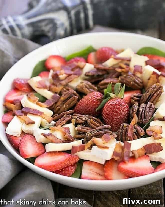 Freshly prepared Strawberry Bacon Brie Salad in a elegant white serving bowl, showcasing vibrant strawberries, crispy bacon, and creamy brie atop a bed of spinach.