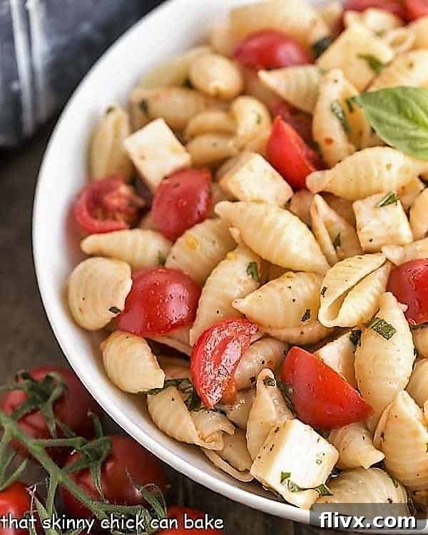 A close-up view of Tomato Basil Pasta Salad with Mozzarella & Fontina in a white serving bowl, highlighting the fresh ingredients and creamy cheese.