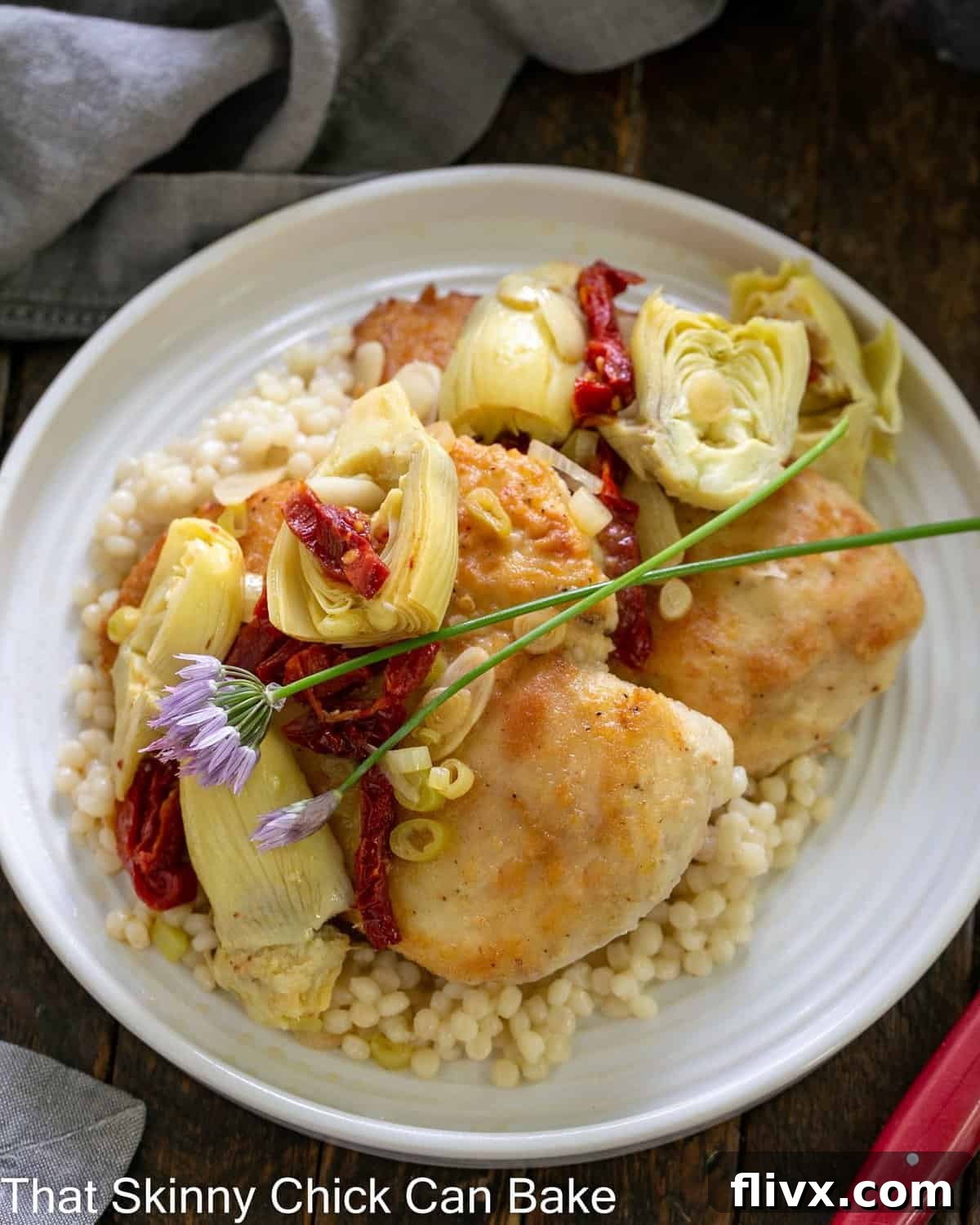 overhead view of chicken with artichokes on a white plate, showcasing the pearl couscous beneath.