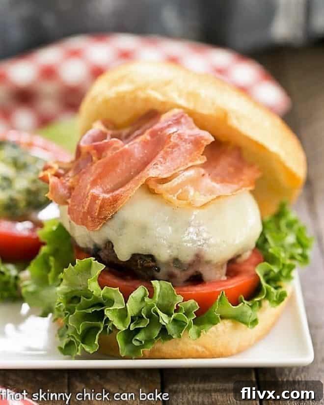 Close up view of Italian Pesto Burger with toppings, including melted mozzarella and crispy prosciutto, on a square plate, showcasing its delicious appeal.