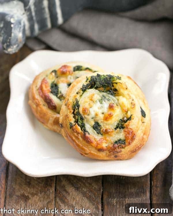 Three perfectly baked Spinach Feta Pinwheels resting on a pristine white square plate, showcasing their golden-brown crust and spiral filling.